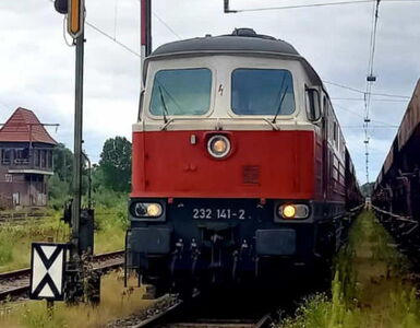 Grossansicht einer rot-weißen Diesellok die an der Signalanlage wartet