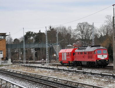 Hilfszug - Diesellock mit angehängtem Betriebswagen in Bahnhofsumgebung eines ländlichen Bahnhofs. Im Hintergrund sind ein Stellwerkhaus und eine Gleisüberquerungsbrücke zu sehen.