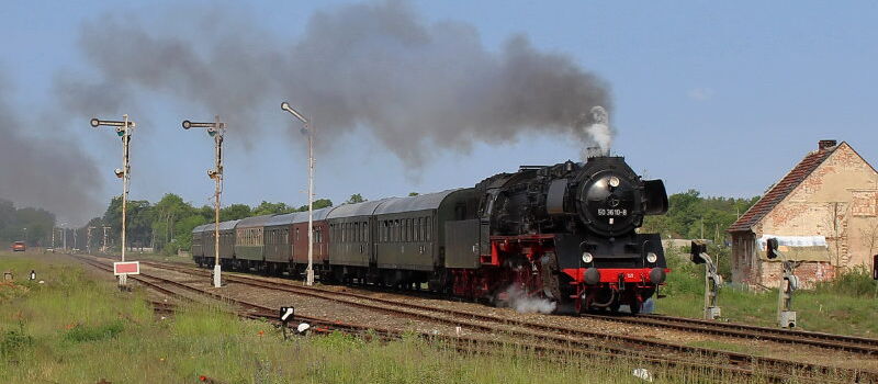 WFL Dampflokzug mit historischen Wagons fährt bei voller Fahrt und Dampf durch Landschaft
