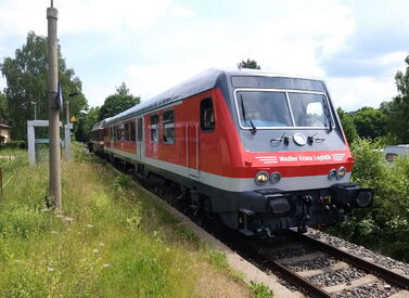 Roter ÖPNV Zug fährt durch grüne Landschaft mit Bäumen.