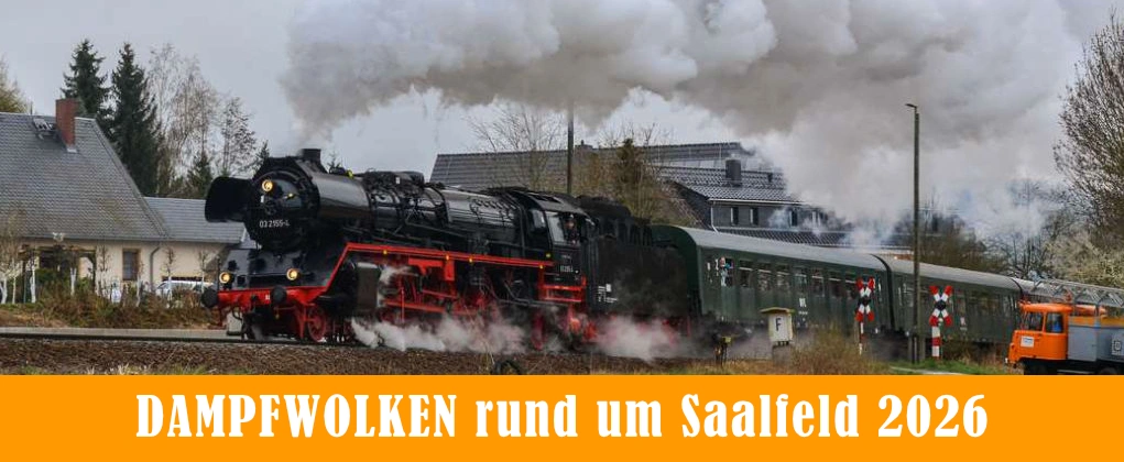 Dampflok Sonderzug fährt unter Volldampf an beschranktem Bahnübergang vorbei